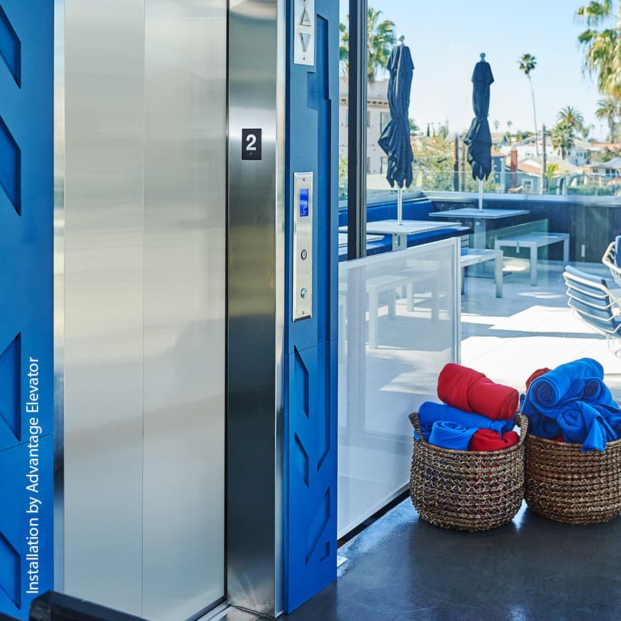 Modern Orion MRL elevator featuring stainless steel doors and custom blue finish on an outdoor balcony.