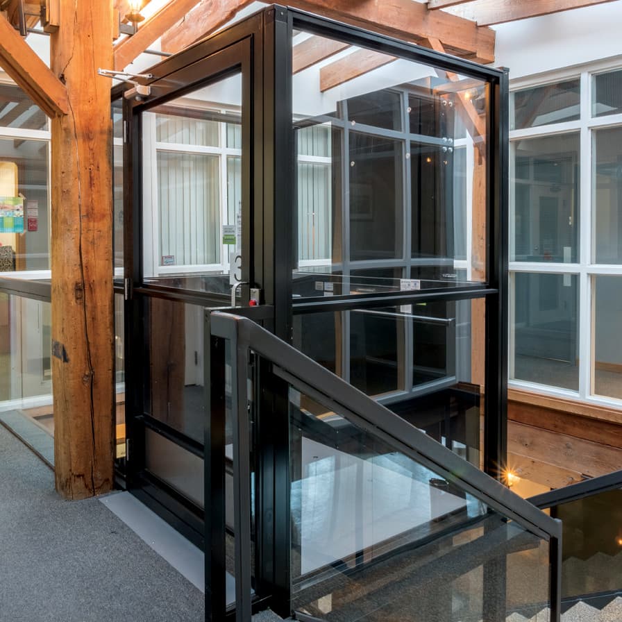 V-1504 vertical platform lift with black frame and glass enclosure in commercial timber-frame building