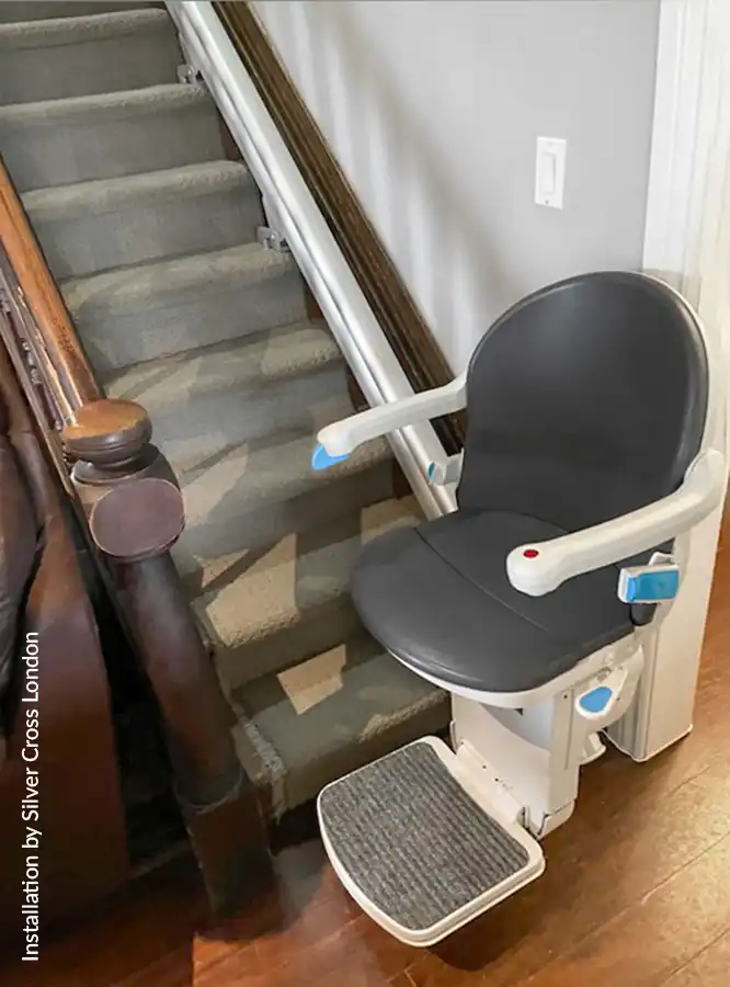 Savaria Handicare 1000 straight stairlift with Smart Seat in slate upholstery, power swivel, aluminum rail with hidden gear rack, and non-slip footrest at bottom landing on carpeted stairs
